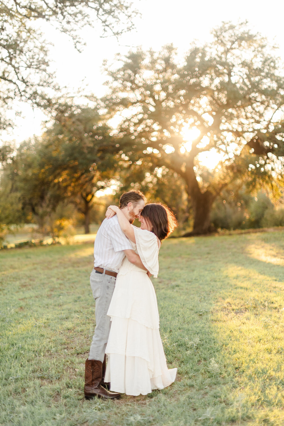 A couple dressed in white embraces with a live oak tree in the background