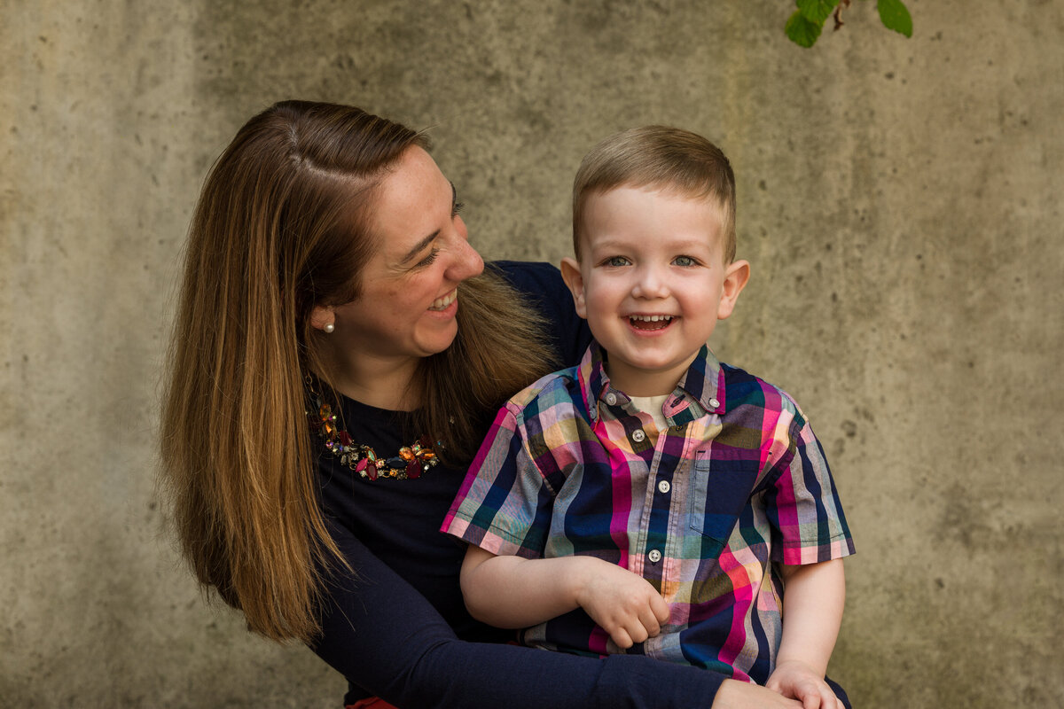 A mom and son laughing together on a simple background, adding a seasonal touch to their Phoenixville mini session.