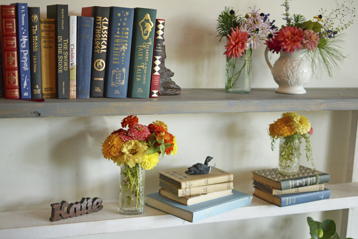 A bookshelf with multicolored books and flowers.