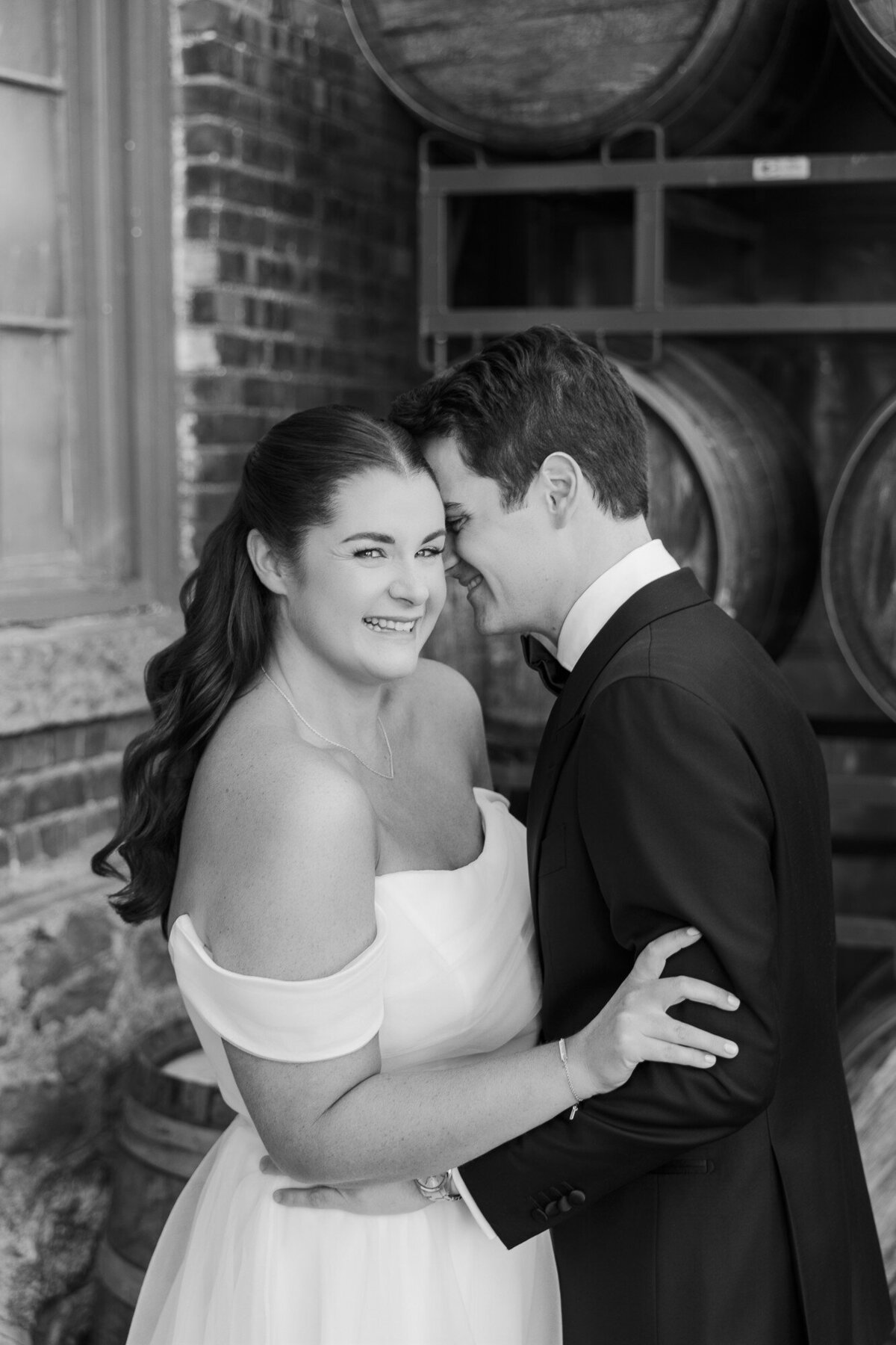 Black and white Hudson Valley wedding portrait of a laughing bride and groom beside wine barrels