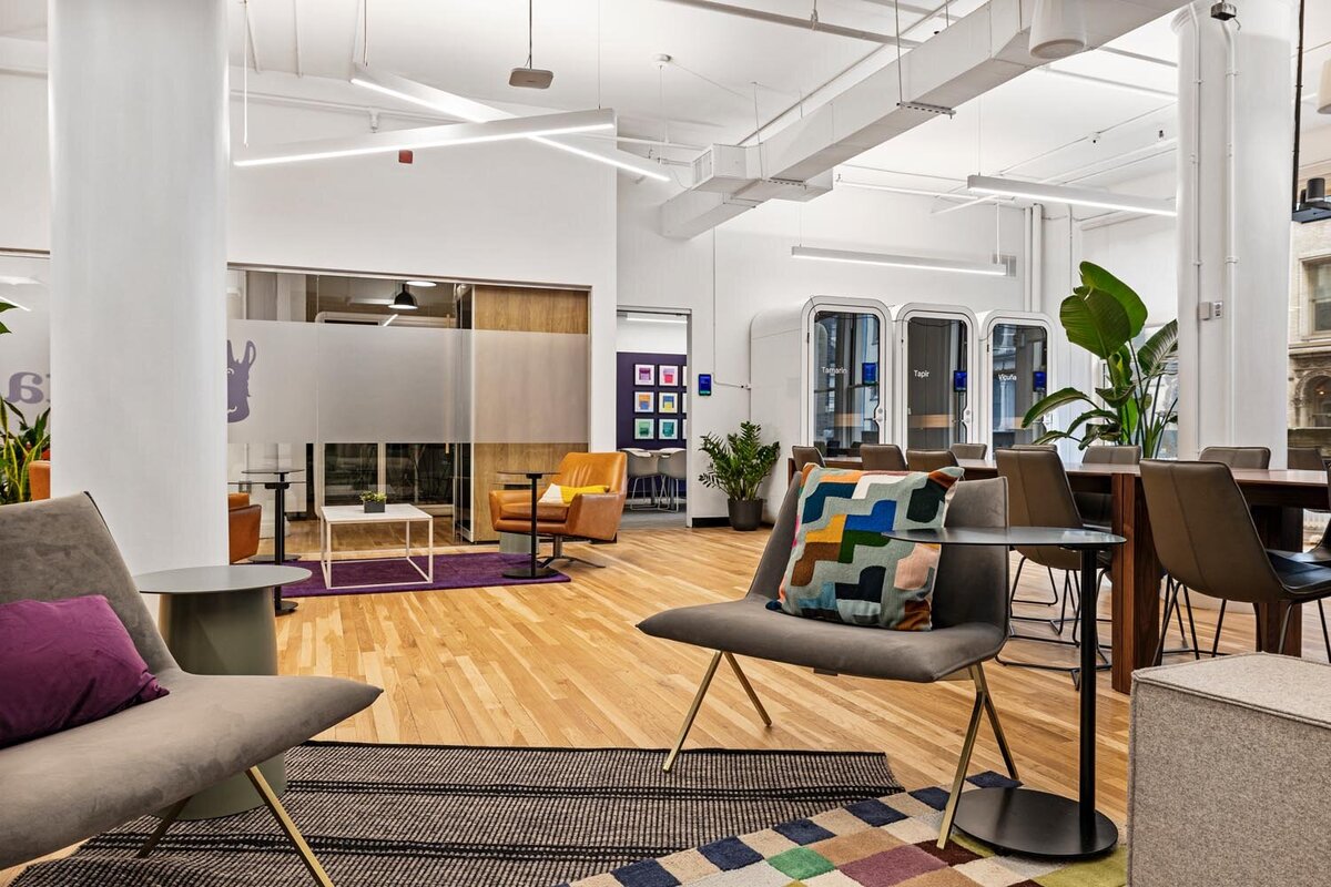 Open office featuring layered seating areas, patterned pillows, greenery, and overhead geometric lighting.