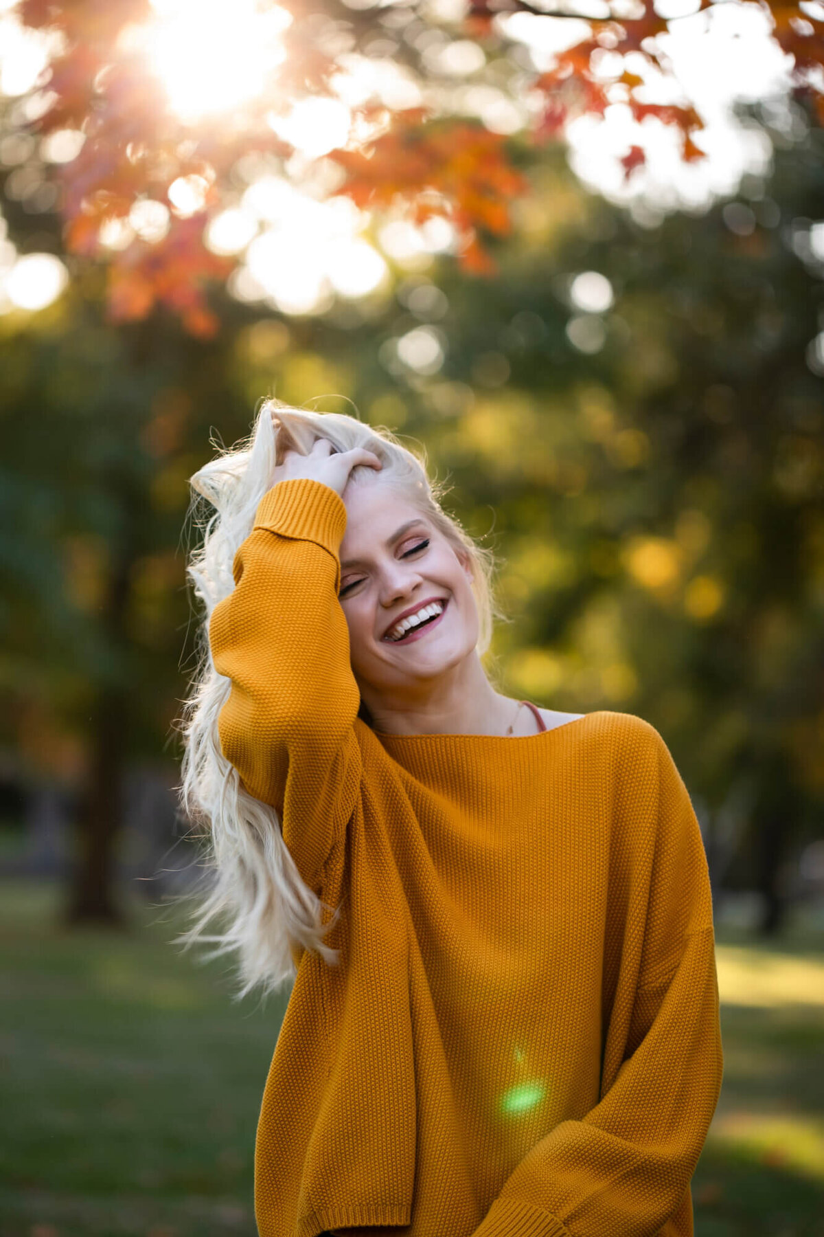 A lovely backlit senior picture of a blonde girl caught off guard laughing and running her hand through her hair. Captured by Springfield, MO senior photographer Dynae Levingston.