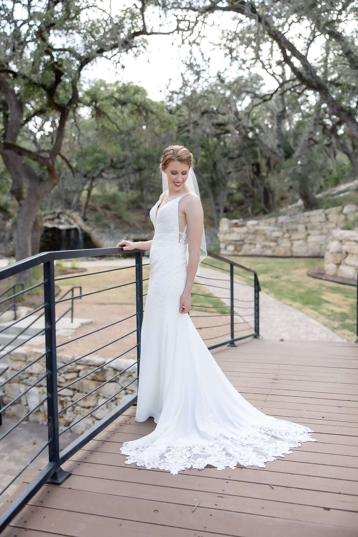 blonde bride looks over lace train on bridge at Hayes Hollow Hidden Falls in Spring Branch Texas