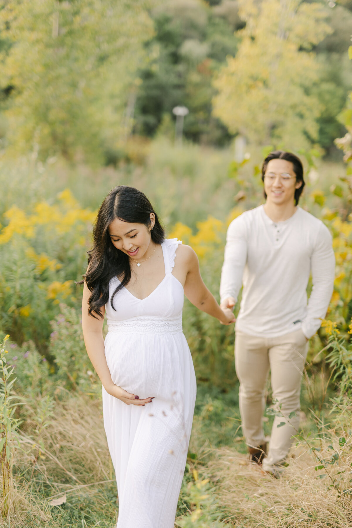 pregnant couple walking in a field by a Toronto Maternity Photographer
