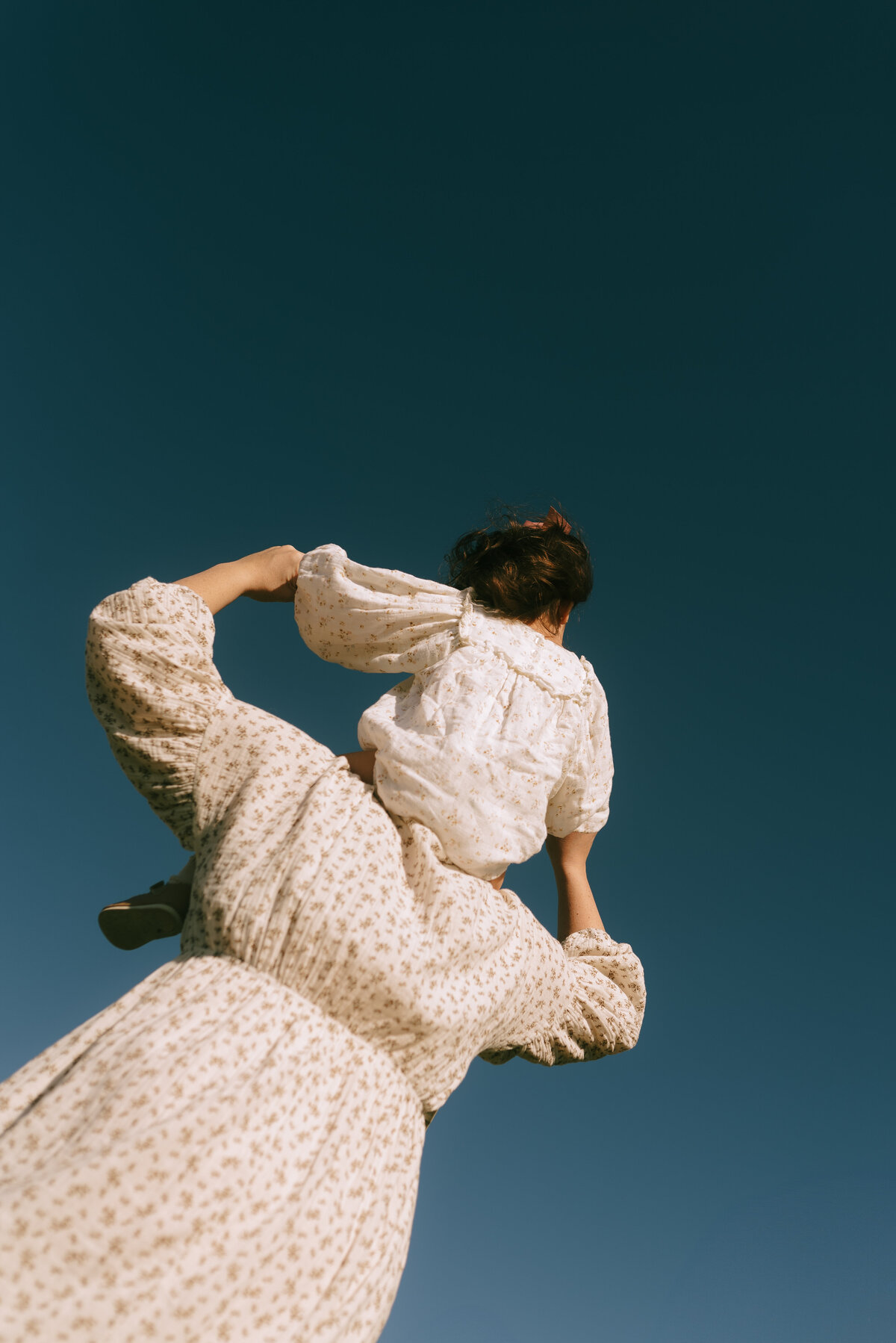 a mother with her daughter on her shoulders with the deep blue sky as their background