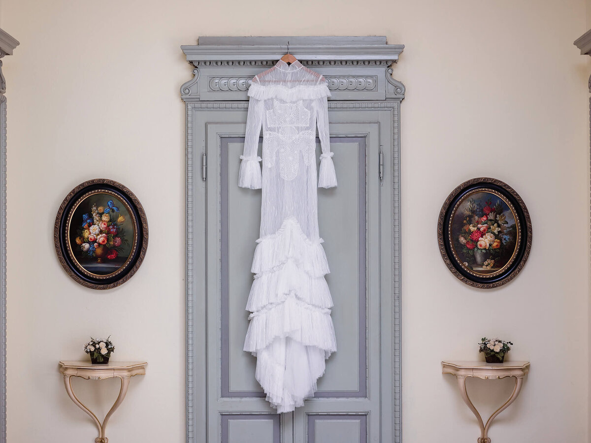 Wedding dress hanging in front of a door; Oval flower paintings on both the sides and console tables with flowers underneath
