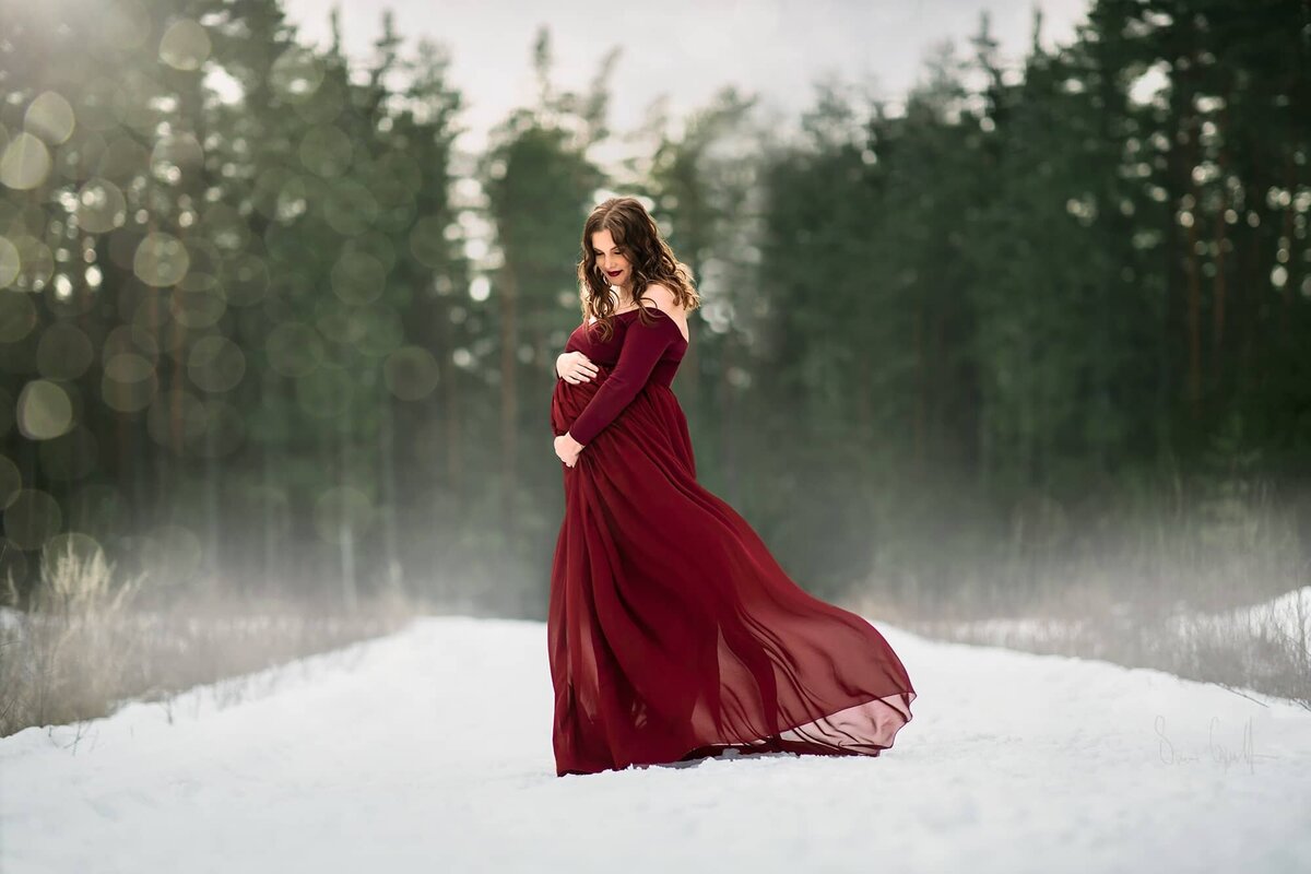 gravidfotografering på skogsväg på vintern. Kvinnan bär en röd klänning.