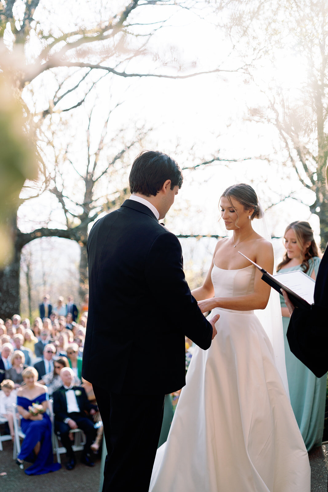 Bride smiling at the groom as they exchange vows during their outdoor wedding ceremony at Burritt on the Mountain in Huntsville, Alabama, photographed by Perry Hancock.