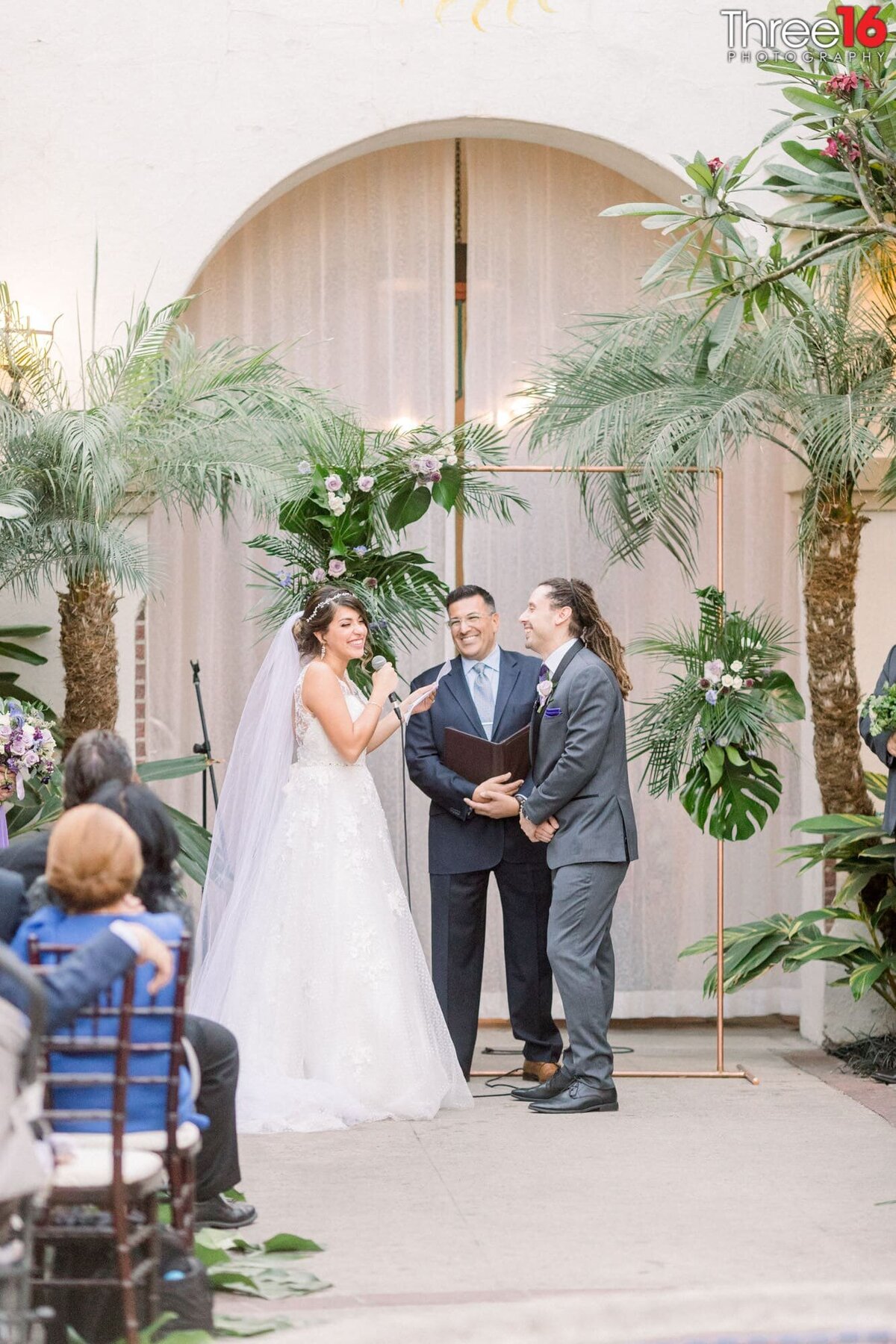 Bride, Groom and officiant start to laugh as she tries to read her vows to him