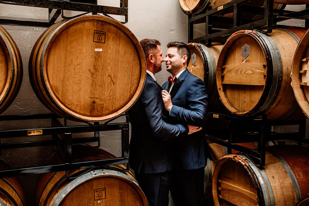 a LGBTQ+ couple, groom and groom standing in a barrel room looking at each other for couples photos during their wedding day