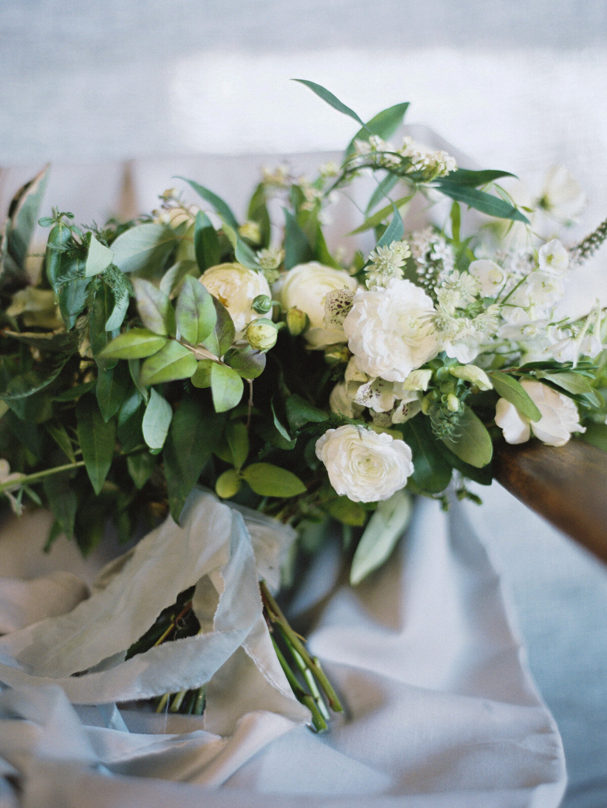 Bouquet of white roses and leaves placed on a wooden chair.