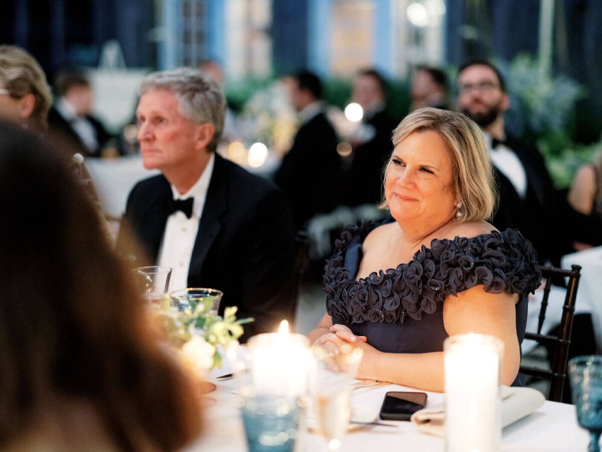 A lovely lady wedding guest is smiling as she watches the program at the reception at Lion Rock Farm, CT. Image by Jenny Fu Studio