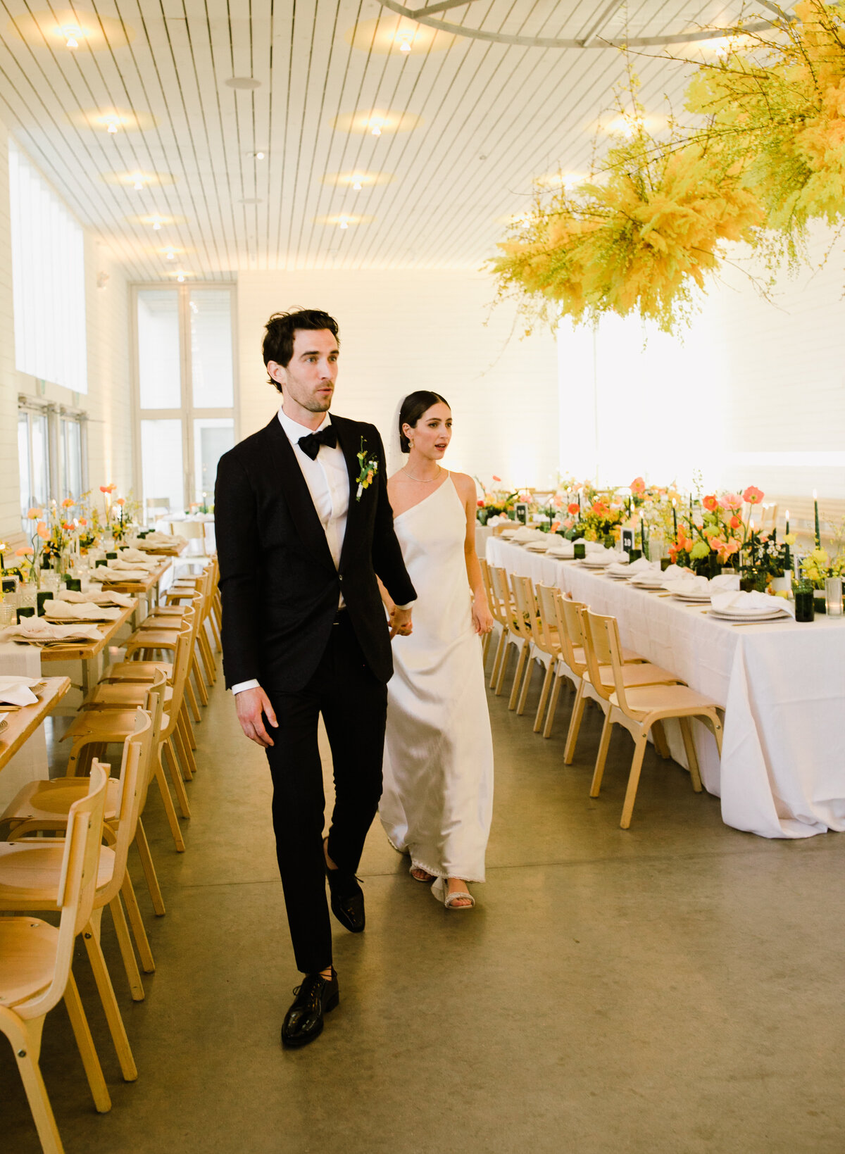 Bride and groom walking between reception tables with bold pops of yellow at Prospect House Austin