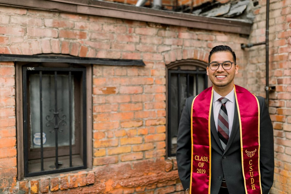 College graduate poses for his grad photos wearing a suit and sash in the back alley in Old Towne Orange