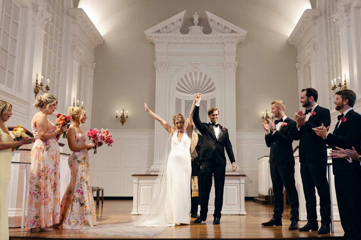 A wedding day photo of the bride and groom with their hands in the air after getting married