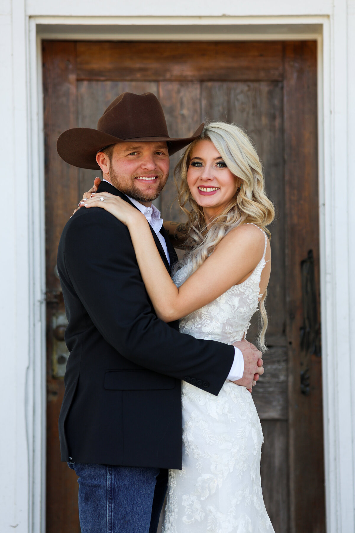 groom wearing Ariat brown cowboy hat and blue jeans and bride wearing white lace dress hugging each other at Crawford Masonic Lodge in Phenix City Alabama by Columbus Georgia wedding photographer Amanda Richardson Photography