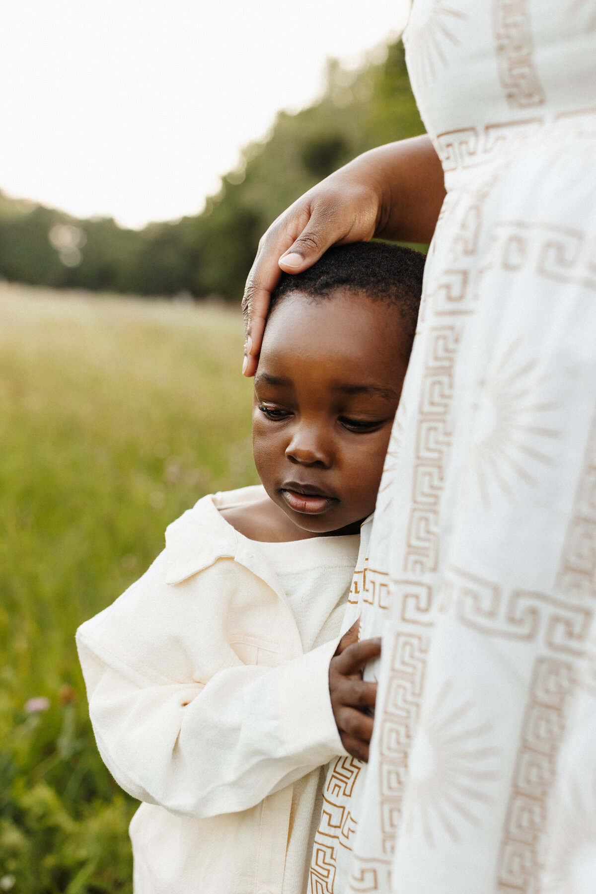 A little boys mother touches her child on the head affectionately while being photographed in the park in christchurch