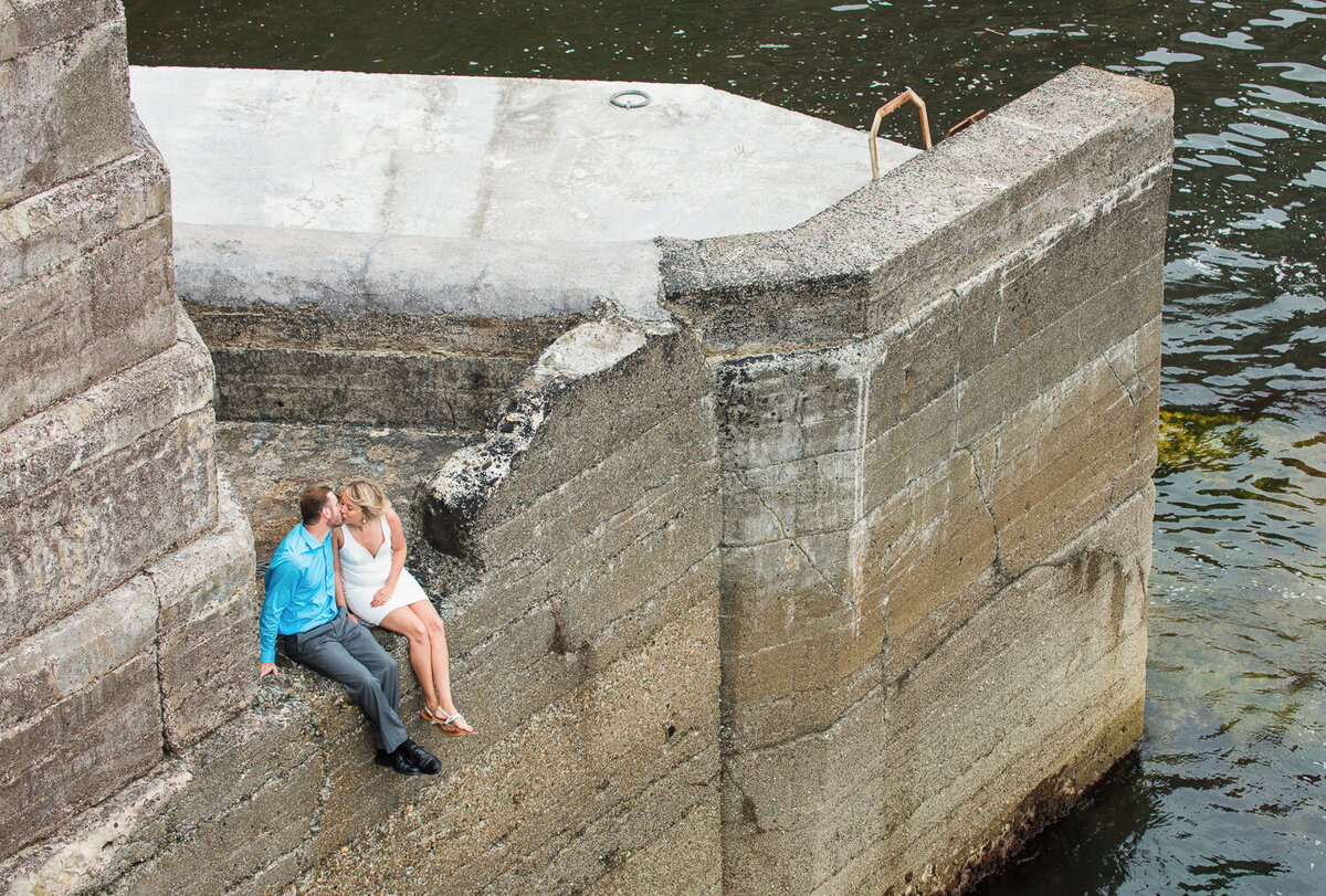Young couple in summer dress sitting on the edge of a deep pier sharing a moment
