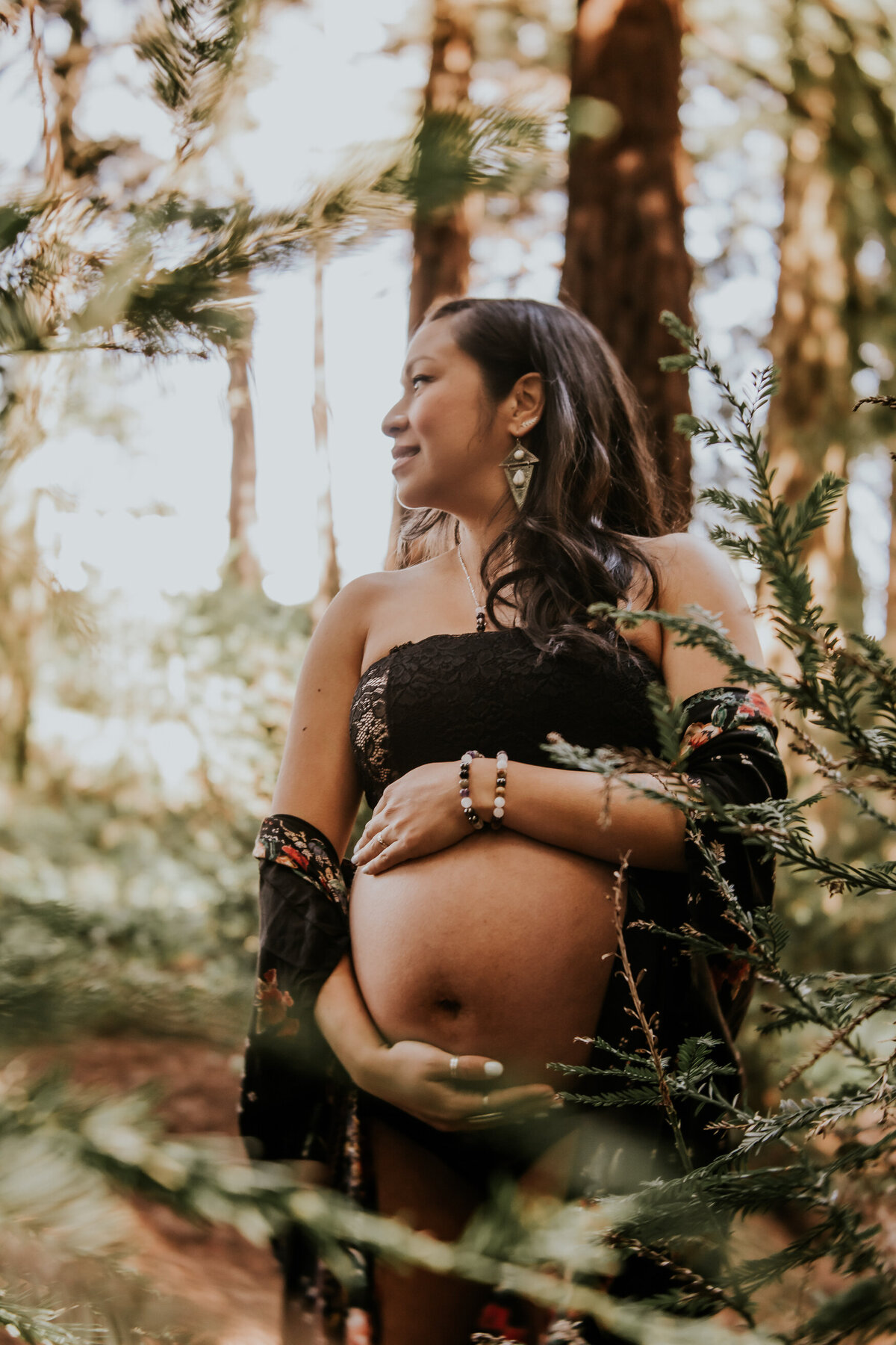 Bohemian San Francisco maternity photography in the redwoods with bare belly pregnanct mom gazing to the side and embracing her belly
