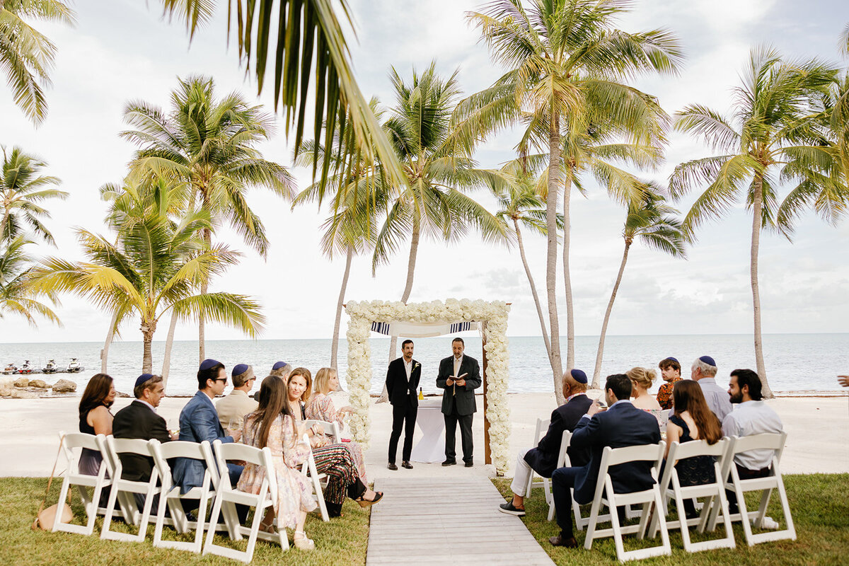 Guests gather under the palm trees for a heartfelt micro wedding ceremony in the Florida Keys. Destination wedding photography by Claudia Amalia.