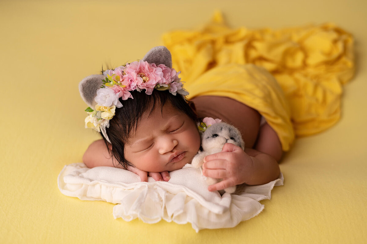 Newborn baby girl with kitty headband holding a kitten posed on her belly on a yellow blanket and wrap and Greater Toronto Photography session.