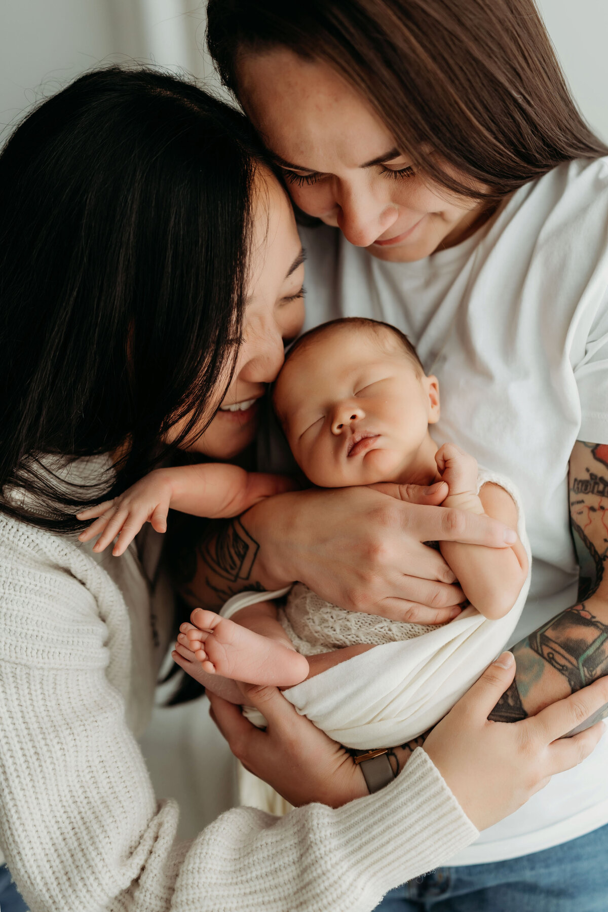 A couple cradles and admires their newborn baby inside a bright all natural light studio