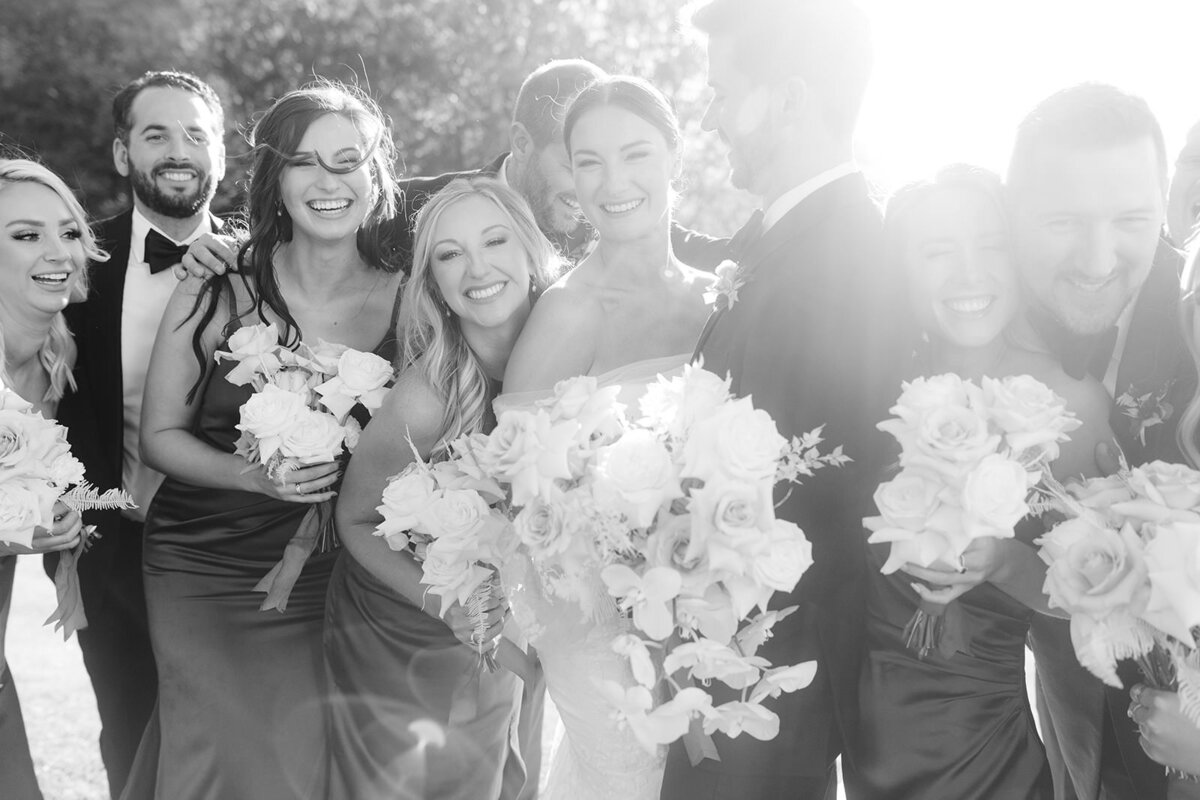 Bride and groom smile joyfully surrounded by their wedding parties