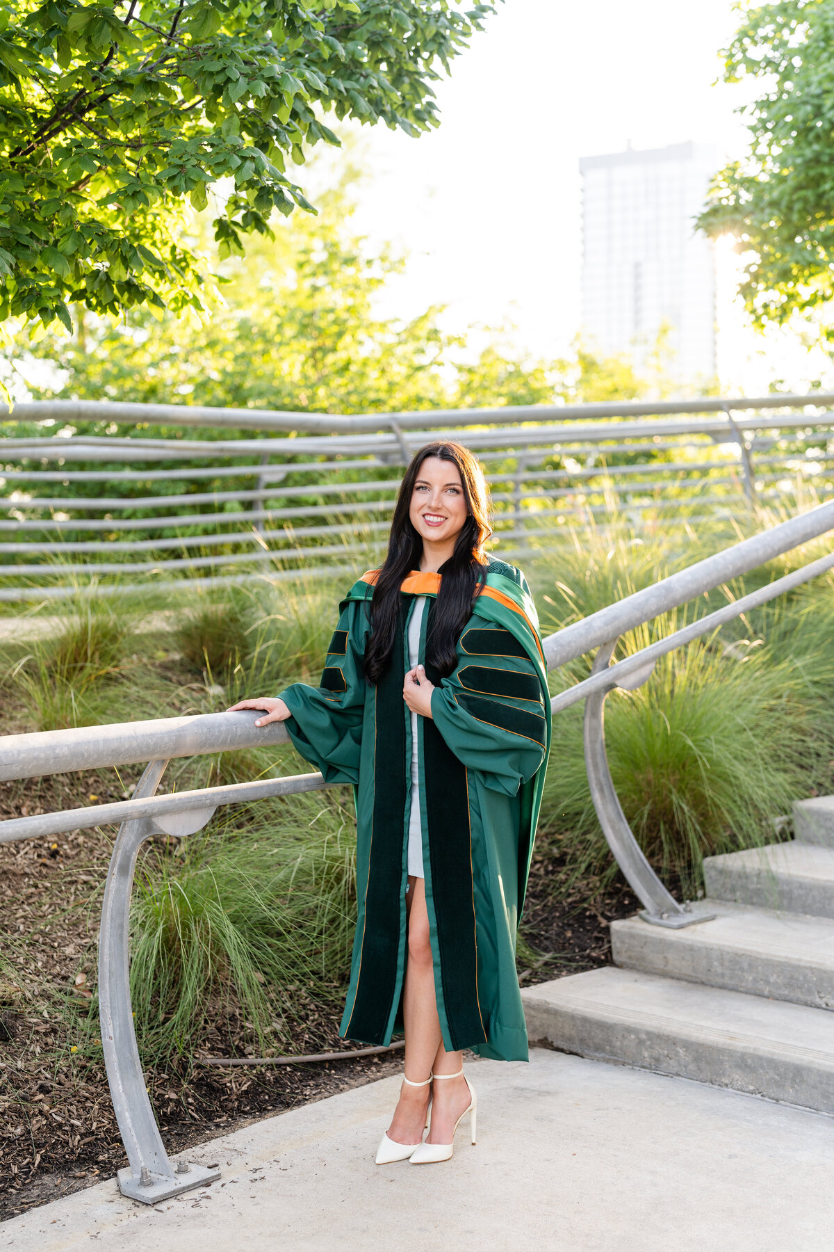 Baylor senior girl wearing doctorate gown and hood while holding gown and hand on railing and smiling in Downtown Houston