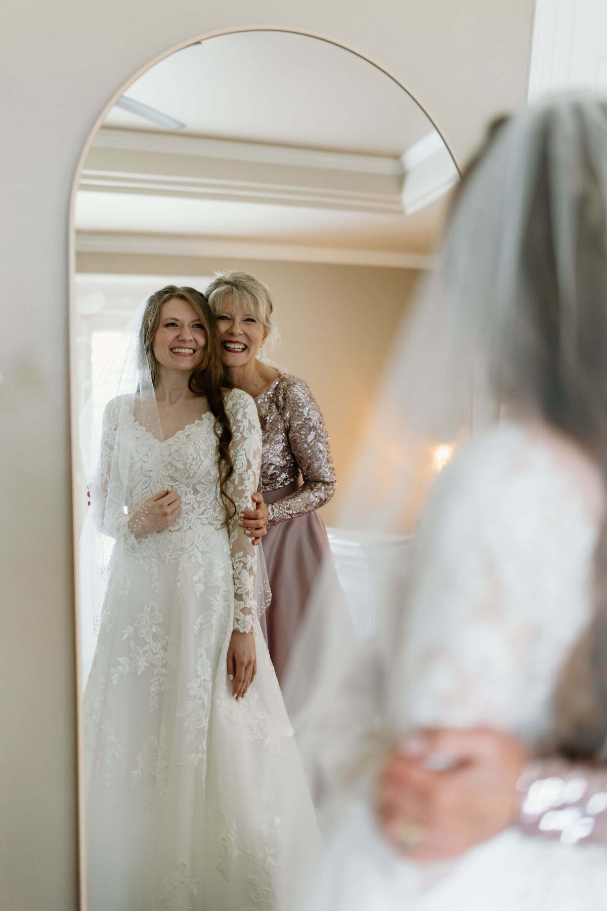 Mother of bride and bride lookin at bride in mirror after putting on wedding dress and veil before East TX wedding ceremony