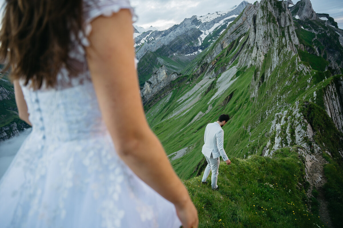 Bride following groom down pathway in mountains in Switzerland