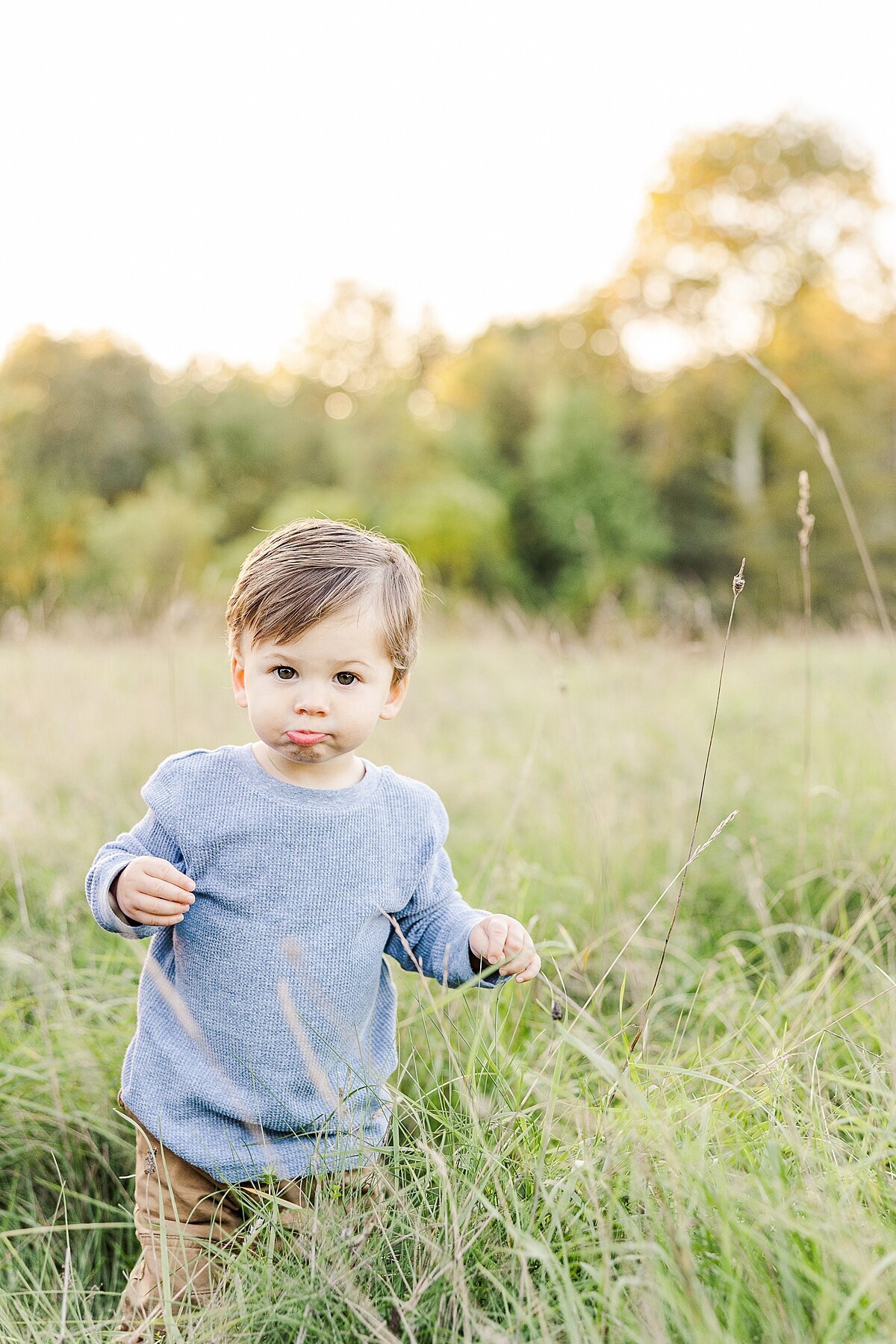 boy stands in field during Family photo session with Sara Sniderman Photography a Oak Grove Park in Millis Massachusetts