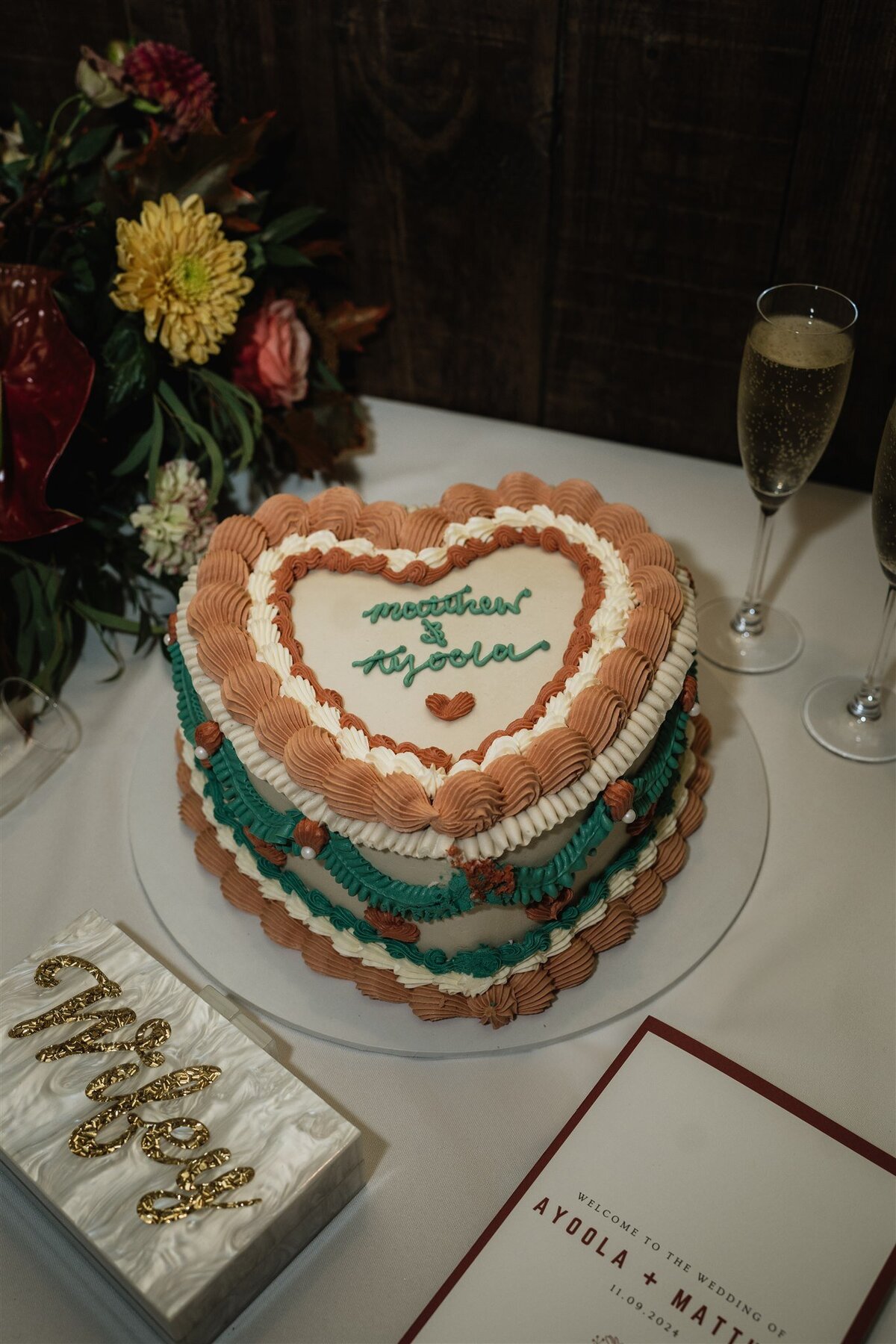 A vintage heart shaped wedding cake sits on a table. Champagne sits beside the cake.