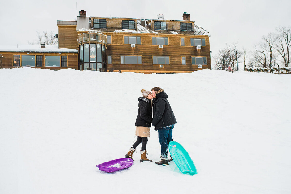 couple kissing in the snow with winter sleds mountain top inn
