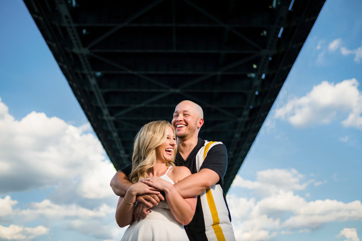 Man and woman, hugging and laughing underneath the race street pier during an engagement session