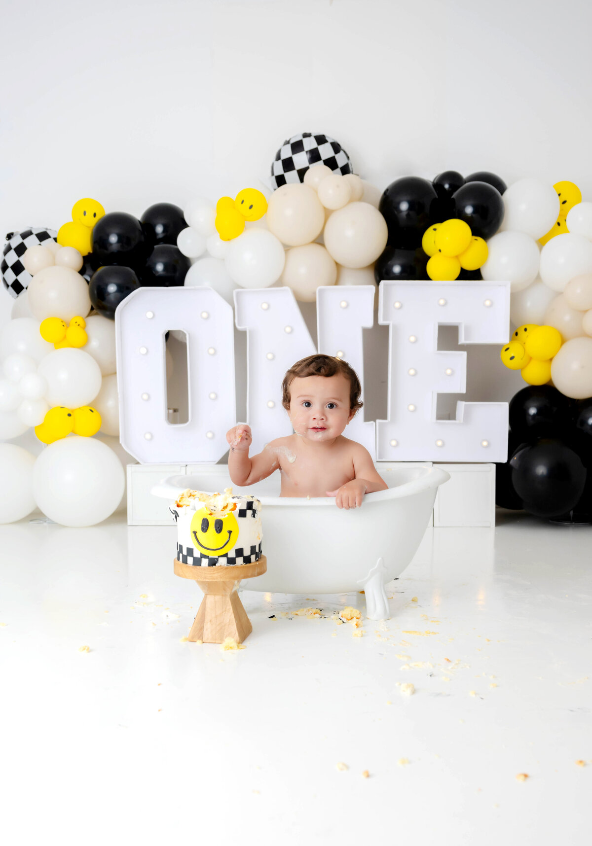 Boy in a minature tub with a giant one and yellow, black and white balloons in the background. 