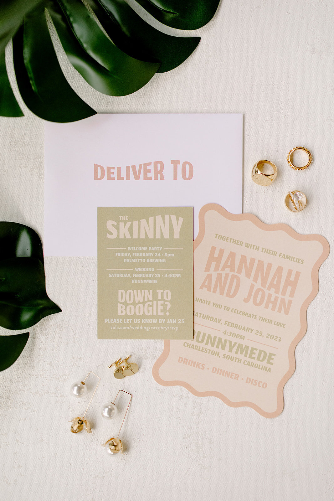 Flat lay of pastel colored wedding invitation suite with rings and earrings