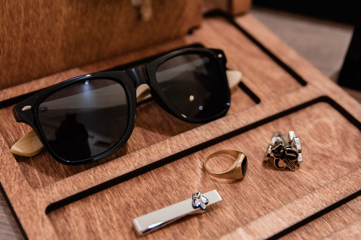 A wooden box containing stylish sunglasses, a sleek watch, and an elegant ring arranged neatly inside. - photo by Jamie Simmons