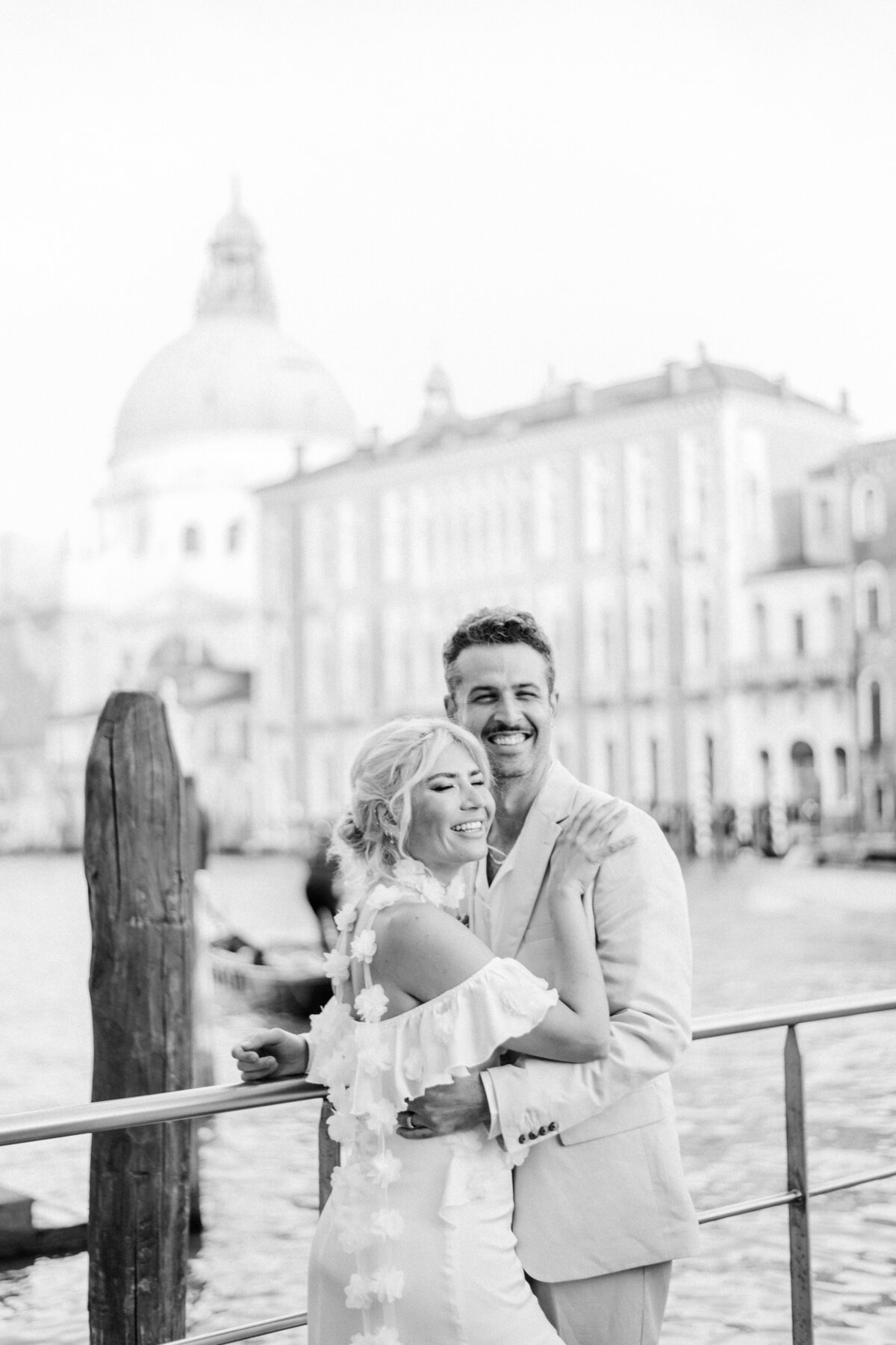 The bride-to-be in a stunning white dress, walking beside her fiancé on the picturesque streets of Venice, captured by Christine Grace.