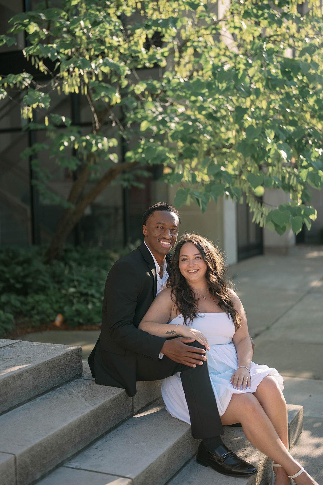 Soft and natural engagement portrait of couple sitting together in shaded garden area.