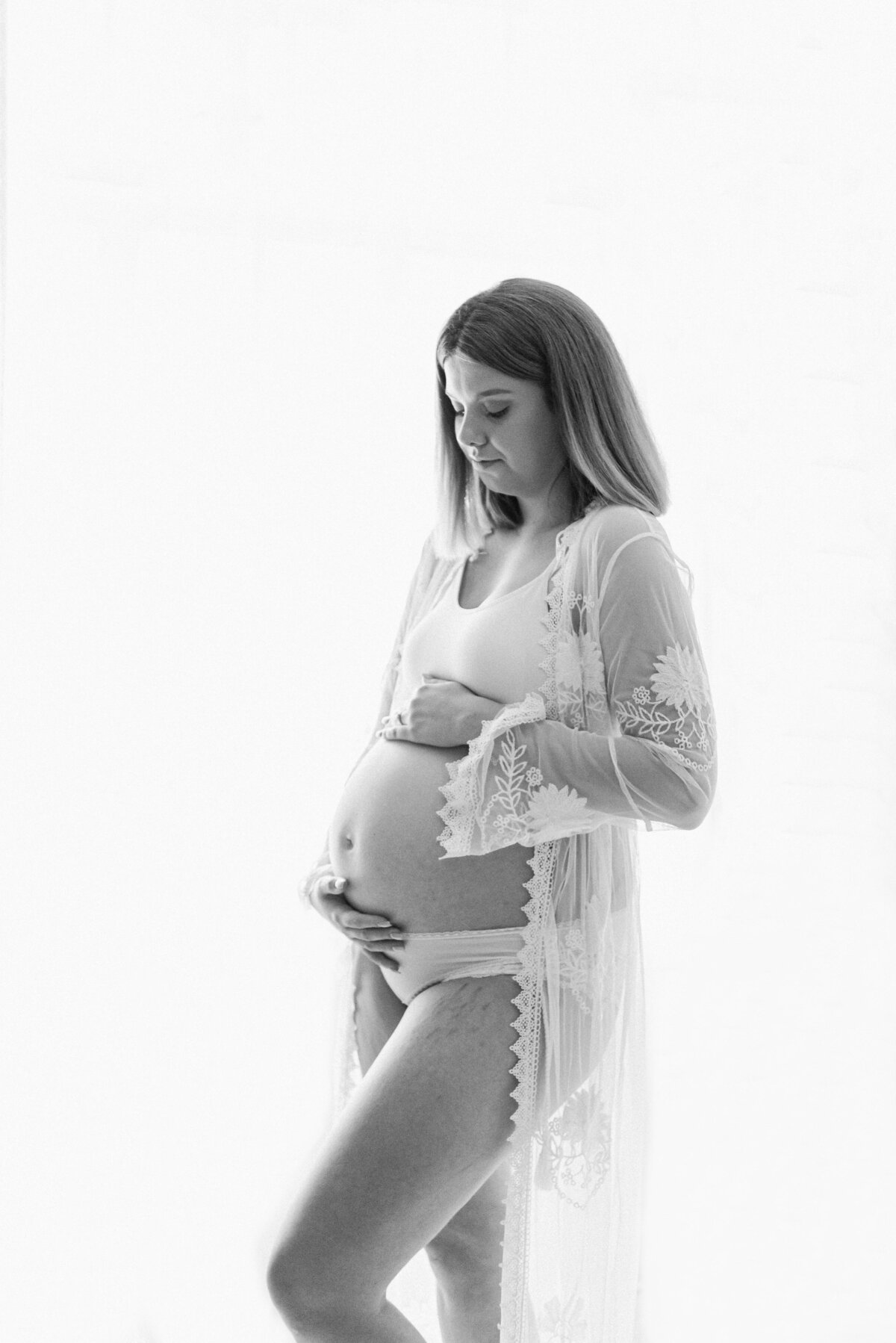 A expecting women holding her bump in all white Billingshurst maternity photography studio