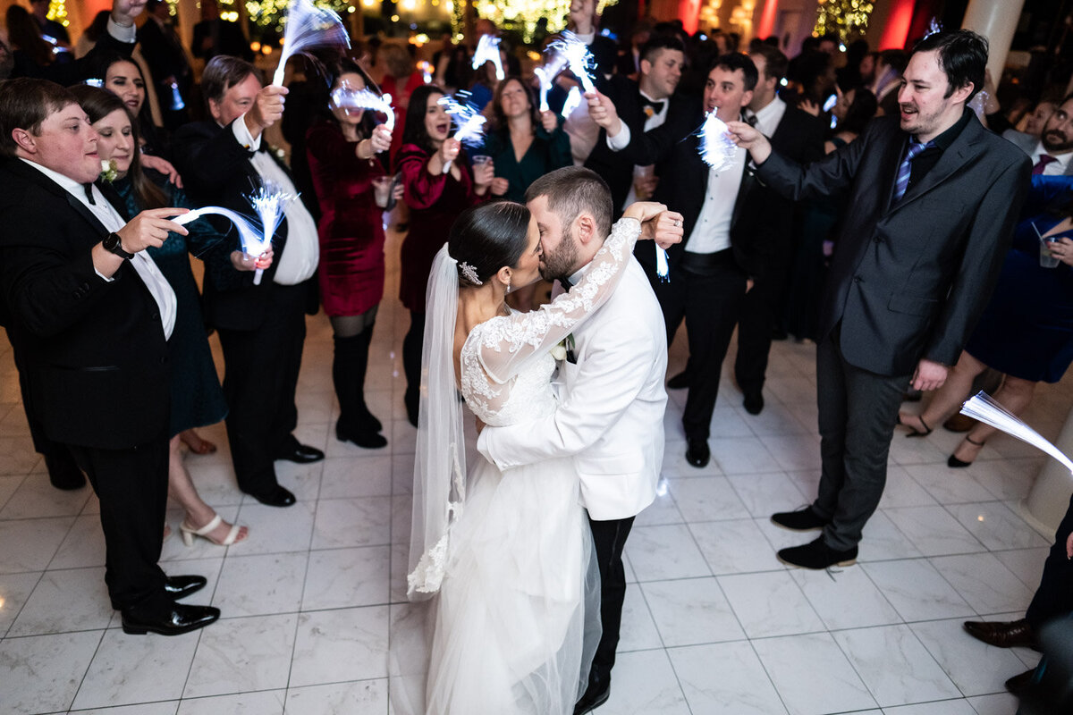 Bride and groom kiss, surrounded by guests at Southern Oaks