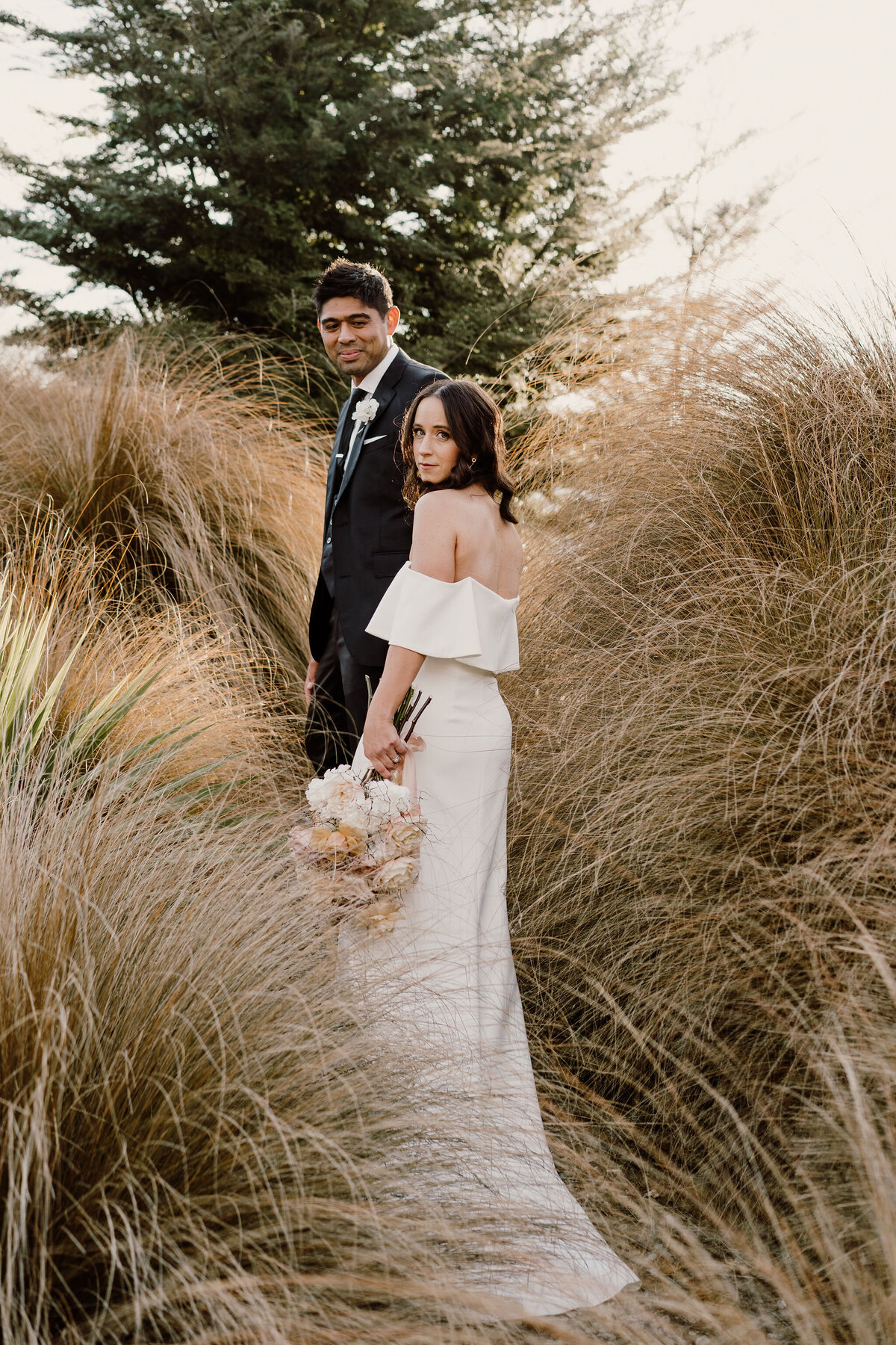 The Vase Floral Co - bride and groom walk through long grass