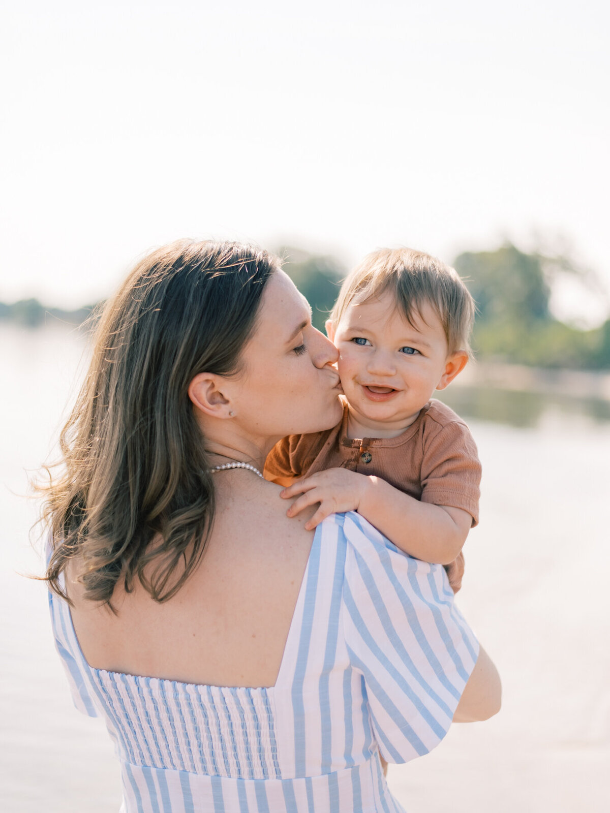 Beautiful mom kissing her little boy in the cheek at beach family session.