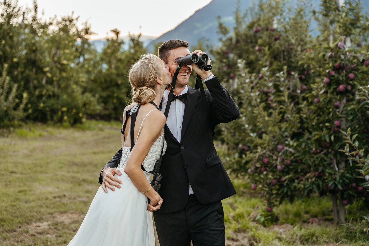 Bride and groom birdwatching with binoculars in orchard
