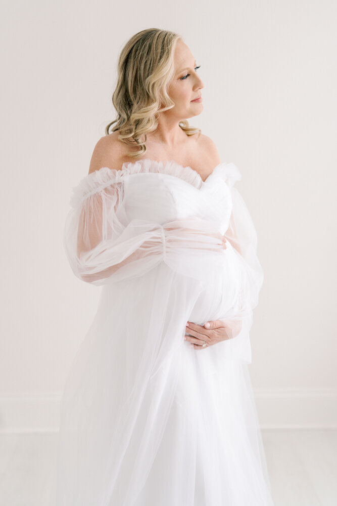 pregnant-mom-in-white-gown-gazing-out-window