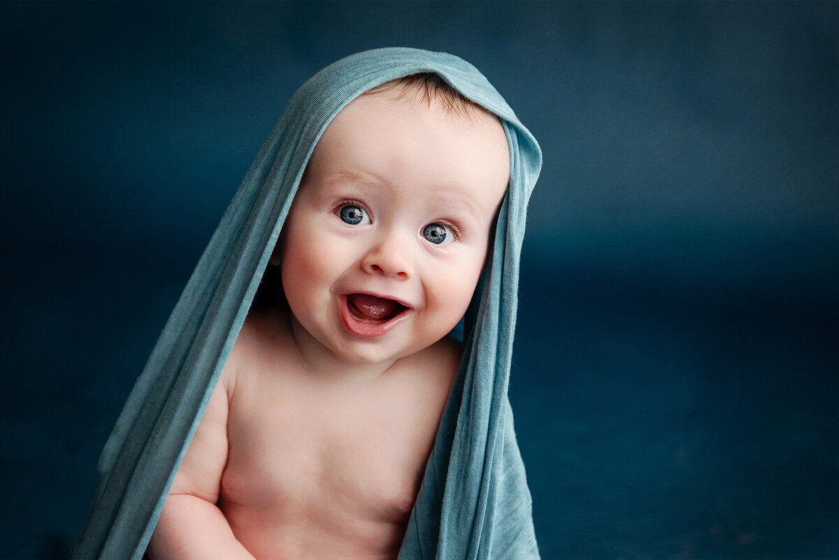 Baby with blue eyes smiling at the camera with a blue cloth on his head
