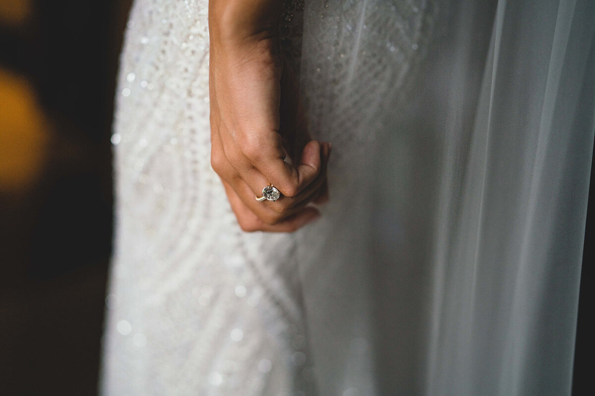 Close-up photograph of the brides wedding ring against her berta wedding dress