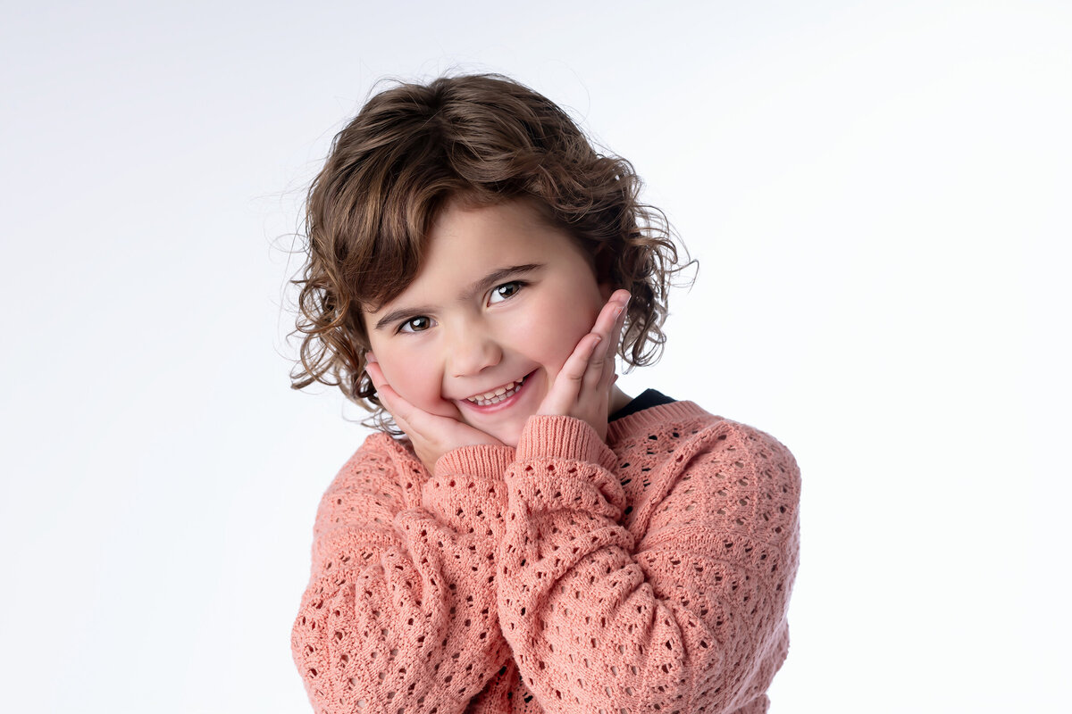 Little girl acts silly in a pink sweater on a white background