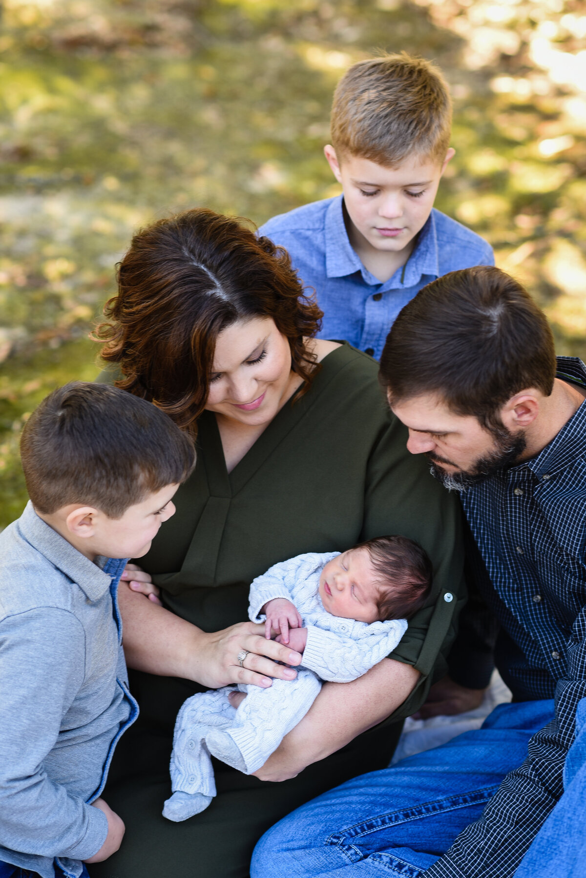 Beautiful Mississippi newborn photography: Family looks down at newborn baby outside under a tree in Mississippi