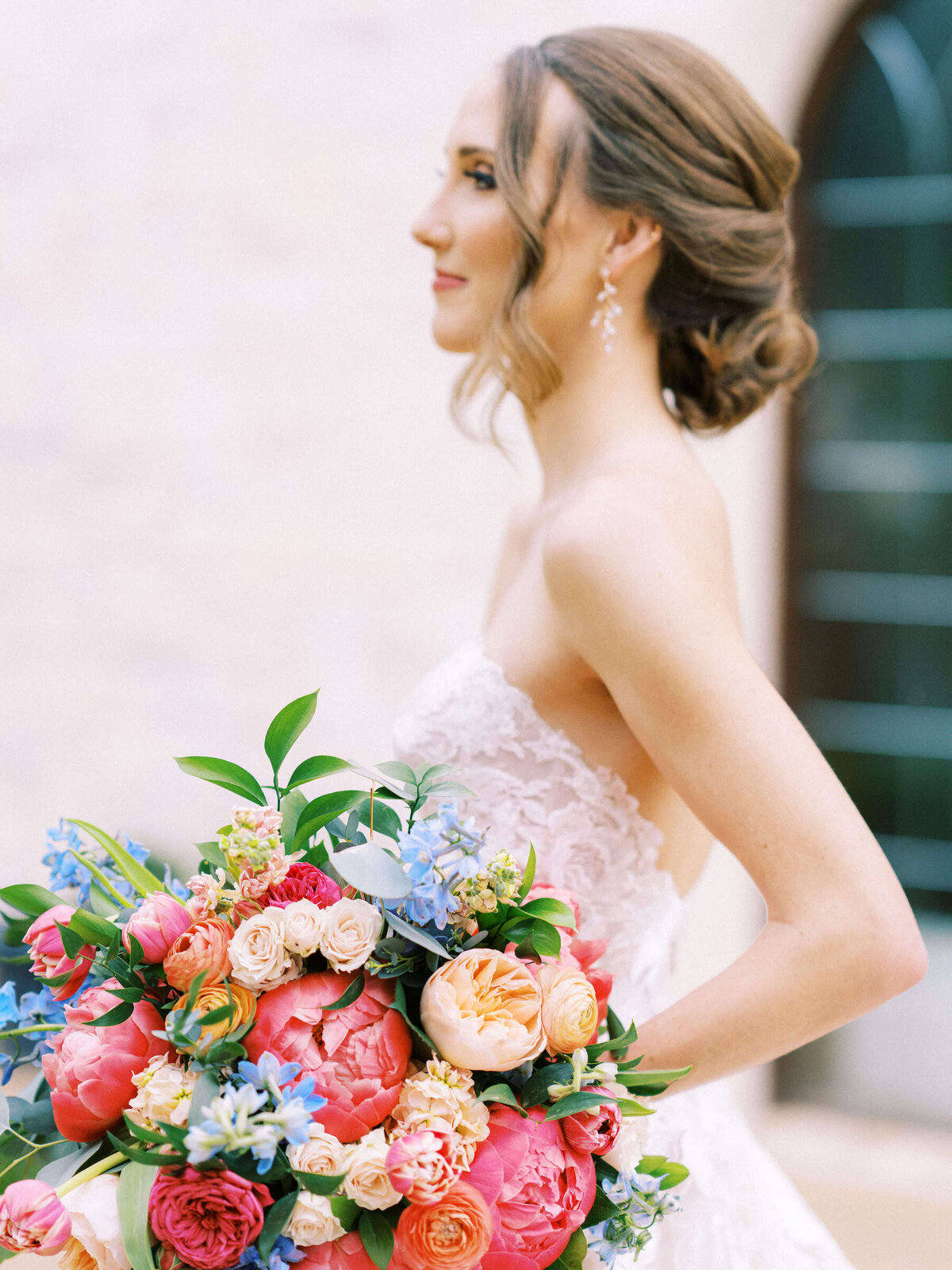 Bride in Monique Lhuillier wedding gown holds her vibrant colorful bridal bouquet